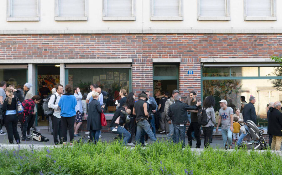 A crowd of people gathers outside a brick building with large glass windows.