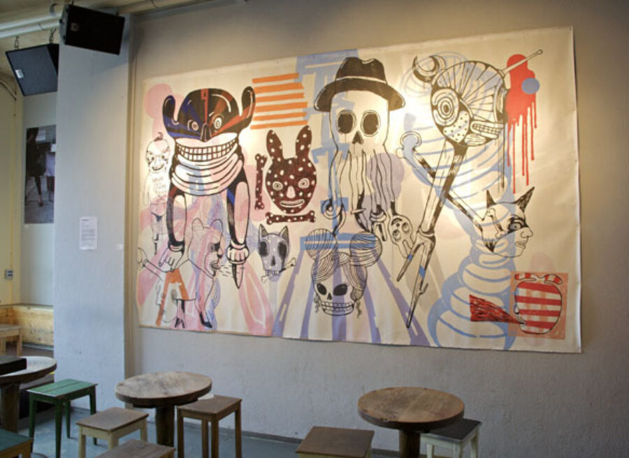 A large canvas with colorful, surrealist sketches of skulls and abstract figures on a grey wall.