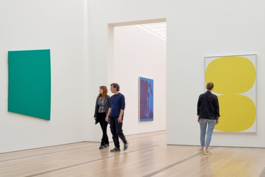 Drei Personen betrachten große, farbige abstrakte Gemälde in einer hellen Galerie.