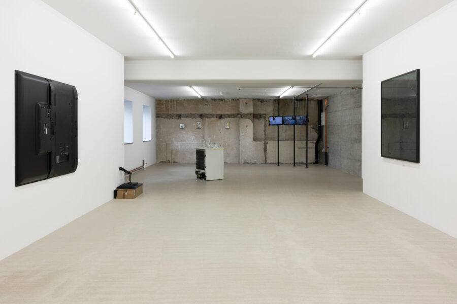 A minimalist art gallery with white walls, featuring digital screens and industrial elements.