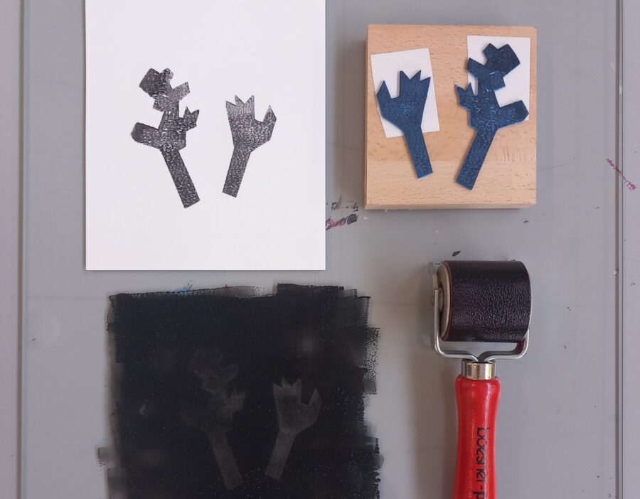 Linocut tools including a carved block, a black print on white paper, and a brayer roller.