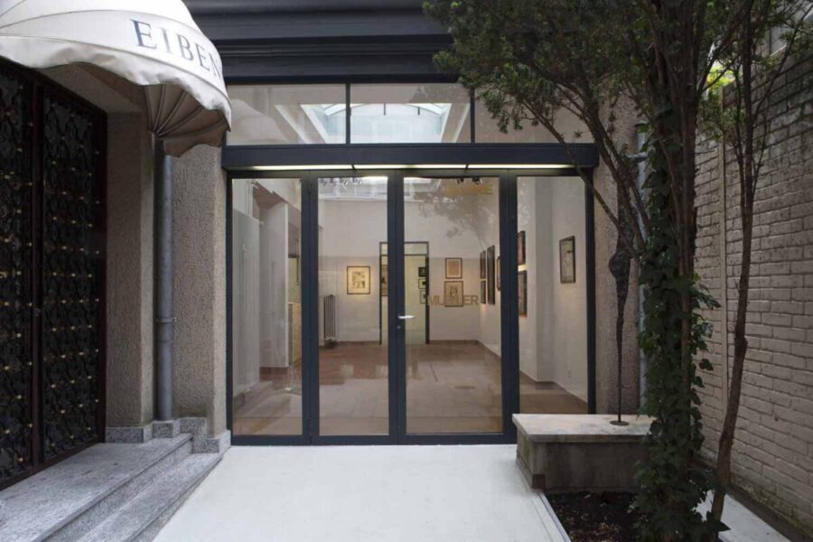 Glass entrance doors lead into a bright art gallery with paintings on white walls.