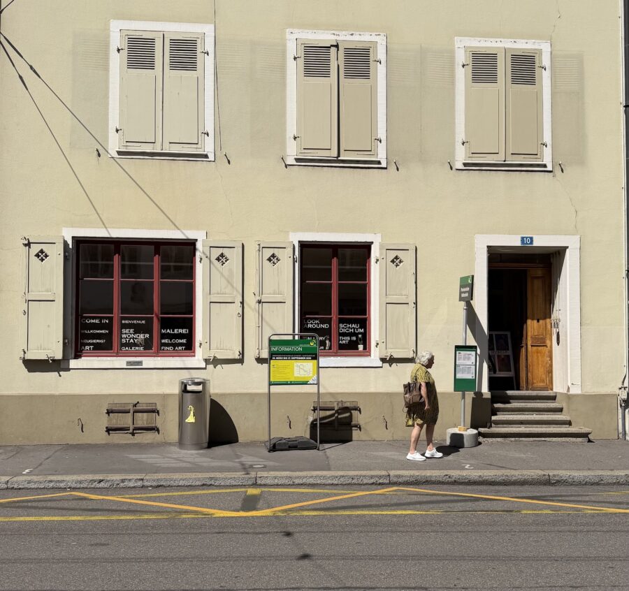 Eine Person steht vor einem hellen Gebäude mit einer Kunstgalerie im Erdgeschoss.
