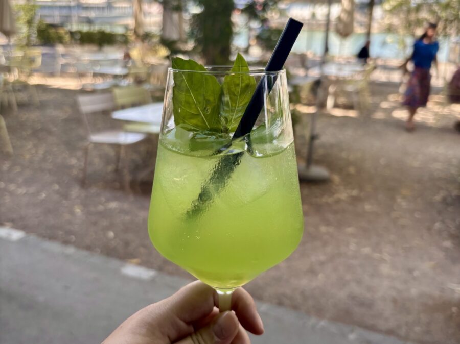 Ein grüner Cocktail mit Eiswürfeln, Basilikumblättern und einem schwarzen Strohhalm in einem Glas.