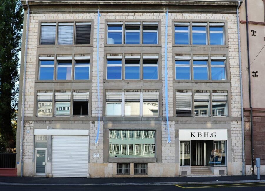 Four-story stone building with large windows and a ground-floor entrance marked KB HG.