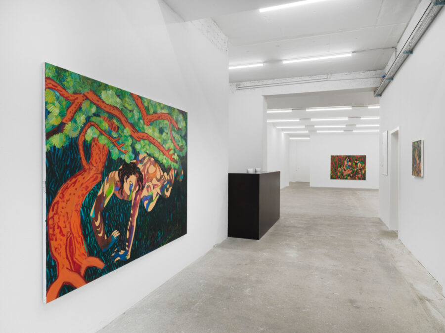 A bright art gallery with white walls, a concrete floor, and colorful paintings on display.