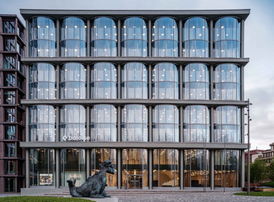 Modernes Bürogebäude mit einer markanten Fassade aus abgerundeten Glasfronten und einer Statue davor.