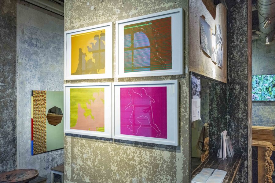 Four colorful abstract art prints in white frames hanging on a textured concrete wall.