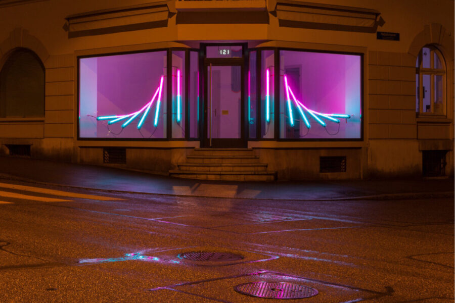 Neon light installation in pink and blue glowing inside a store window at night.