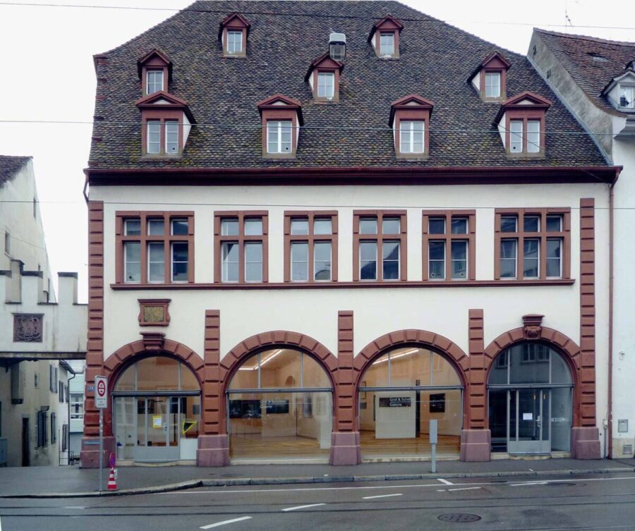 A white three-story building with red stone accents and a brown tiled mansard roof.