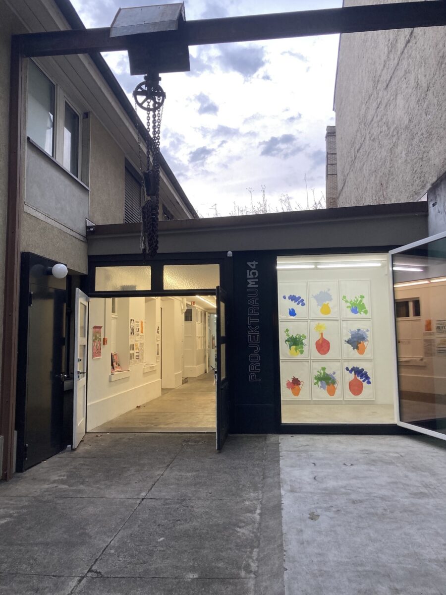 Entrance to the Projektraum 54 gallery, featuring an open door and colorful art in the window.