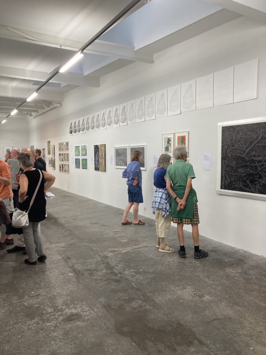 People viewing a series of framed artworks and drawings in a brightly lit art gallery.