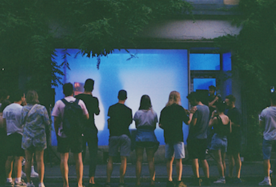 A group of people stand with their backs to the camera, looking at a glowing blue screen.