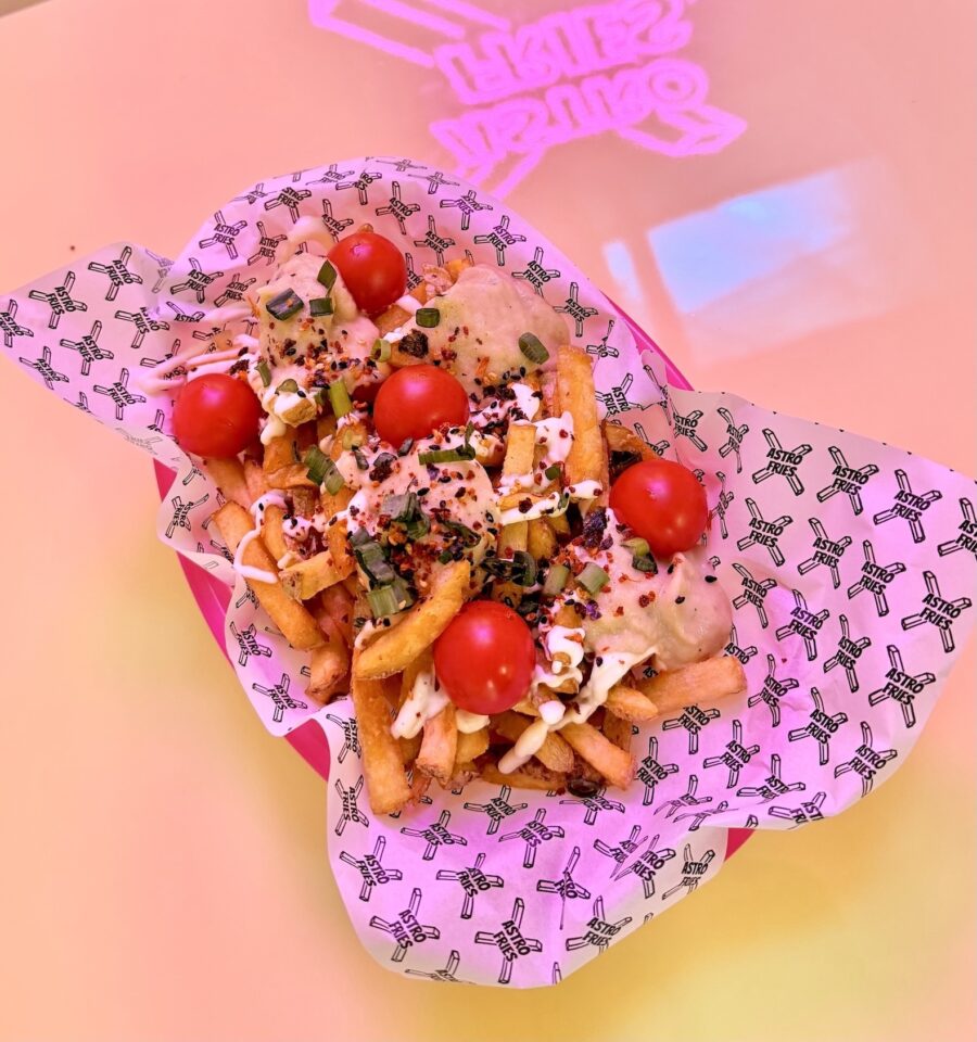 Loaded french fries topped with cherry tomatoes and sauce in a branded paper liner.