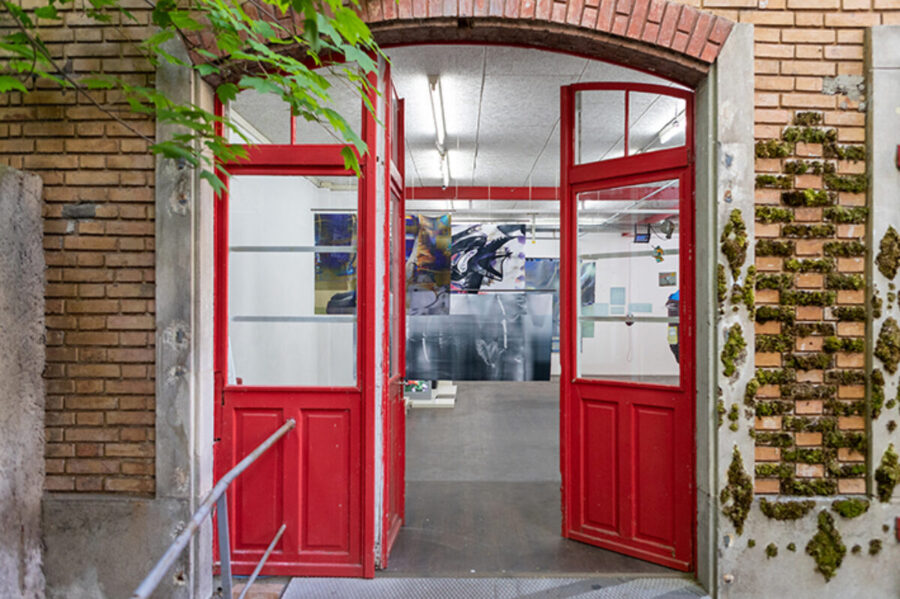 Open red double doors in a brick archway leading into an art studio with hanging paintings.